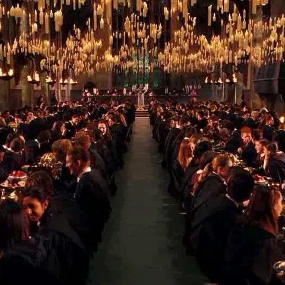 A grand dining hall with long tables filled with people, illuminated by hundreds of floating candles.