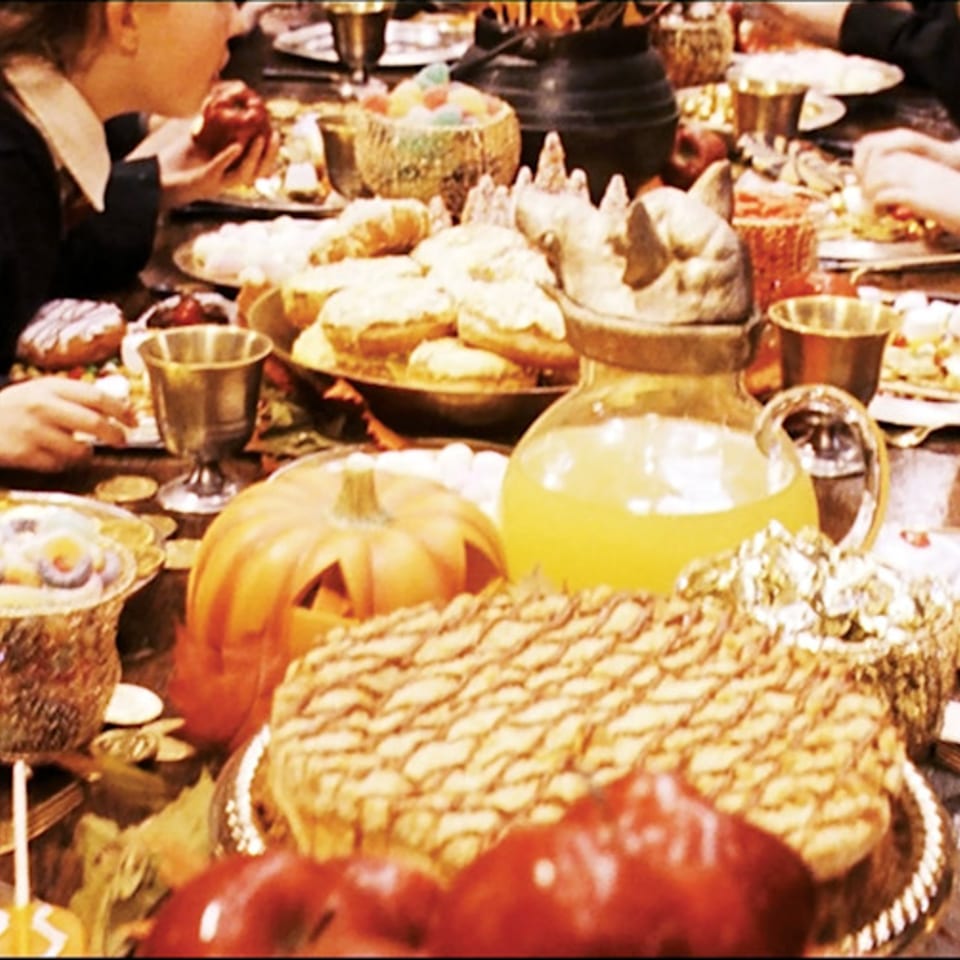 A festive table laden with cakes, pastries, apples, and drinks, with people dining.